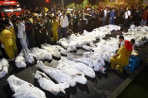 Десятки тел, завернутых в белые простыни, лежат на тротуаре перед сгоревшим ночным клубом