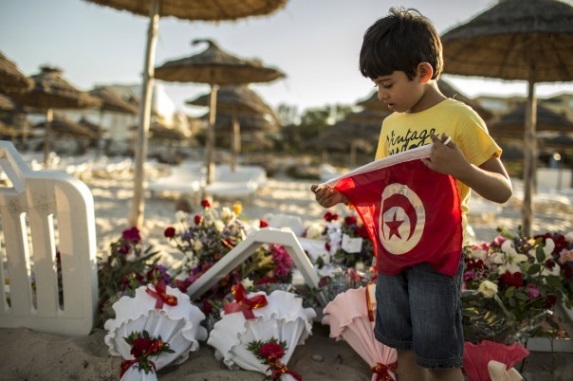 Мальчик держит в руках флаг Туниса, стоя на пляже,  где произошел теракт
