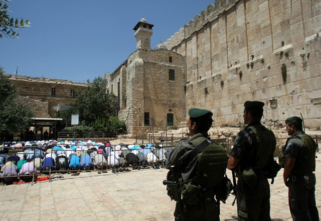Israeli border policemen stand guard as Palestinian men perform the second Friday prayers of the Muslim fasting month of Ramadan outside the Ibrahimi Mosque or the Tomb of the Patriarchs in the West Bank city of Hebron on July 27, 2012. AFP PHOTO / HAZEM BADER        (Photo credit should read HAZEM BADER/AFP/GettyImages)