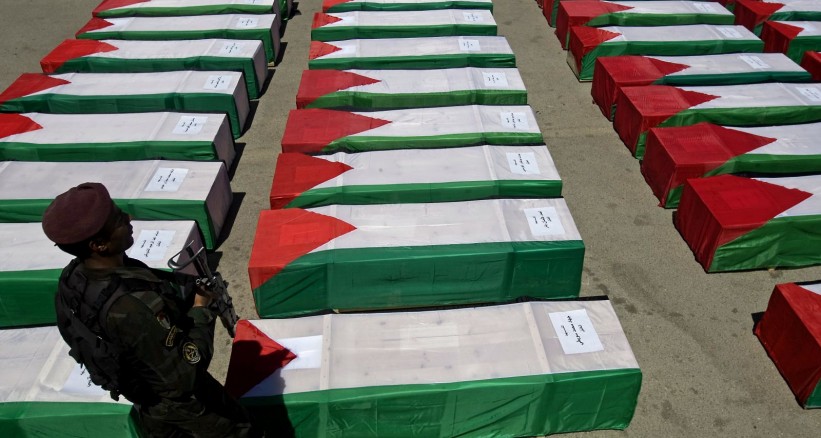 Палестинский военнослужащий на фоне гробов, укрытых национальными флагами