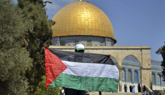 Мужчина стоит возле комплекса «Аль-Акса», держа в руках палестинский флаг