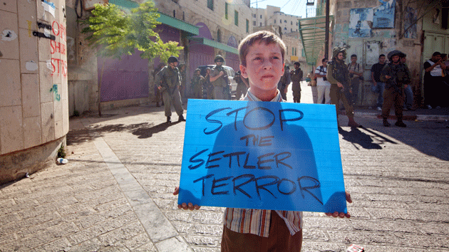 Палестинский ребенок держит плакат с требованием остановить строительство израильских поселений
